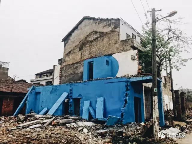 △ 這棟建筑是臨江最近的半拆遷建筑物的遺留，沅江和堤壩成為了展覽的天然背景。創(chuàng)作團(tuán)隊(duì)對(duì)這棟建筑進(jìn)行了半涂裝，將符號(hào)性的沅水曲線與拆遷進(jìn)行中的建筑立面進(jìn)行意義的疊造，它們共同觸發(fā)了場(chǎng)所空間多元語境的生成，把拆遷這種暫時(shí)破壞性、干擾性的介入行動(dòng)與沅水右岸發(fā)展的未來性、美好性緊密融合。